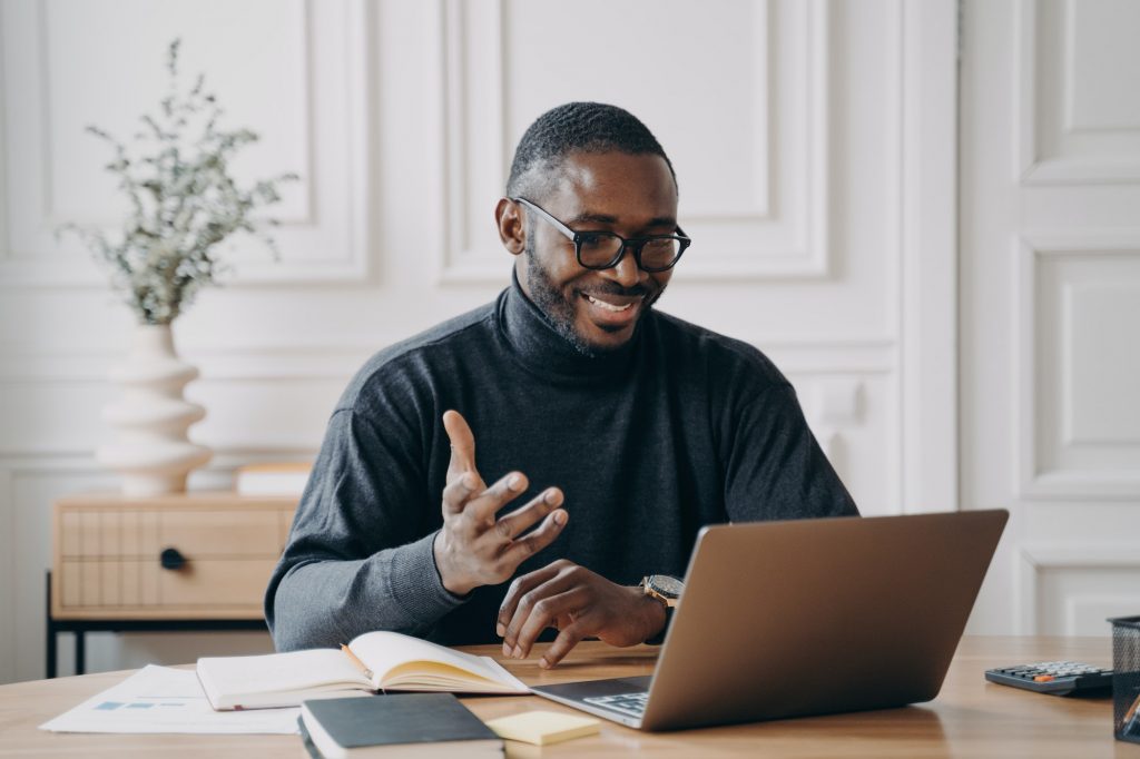 African-American young businessman in glasses having conference online with employes via video call